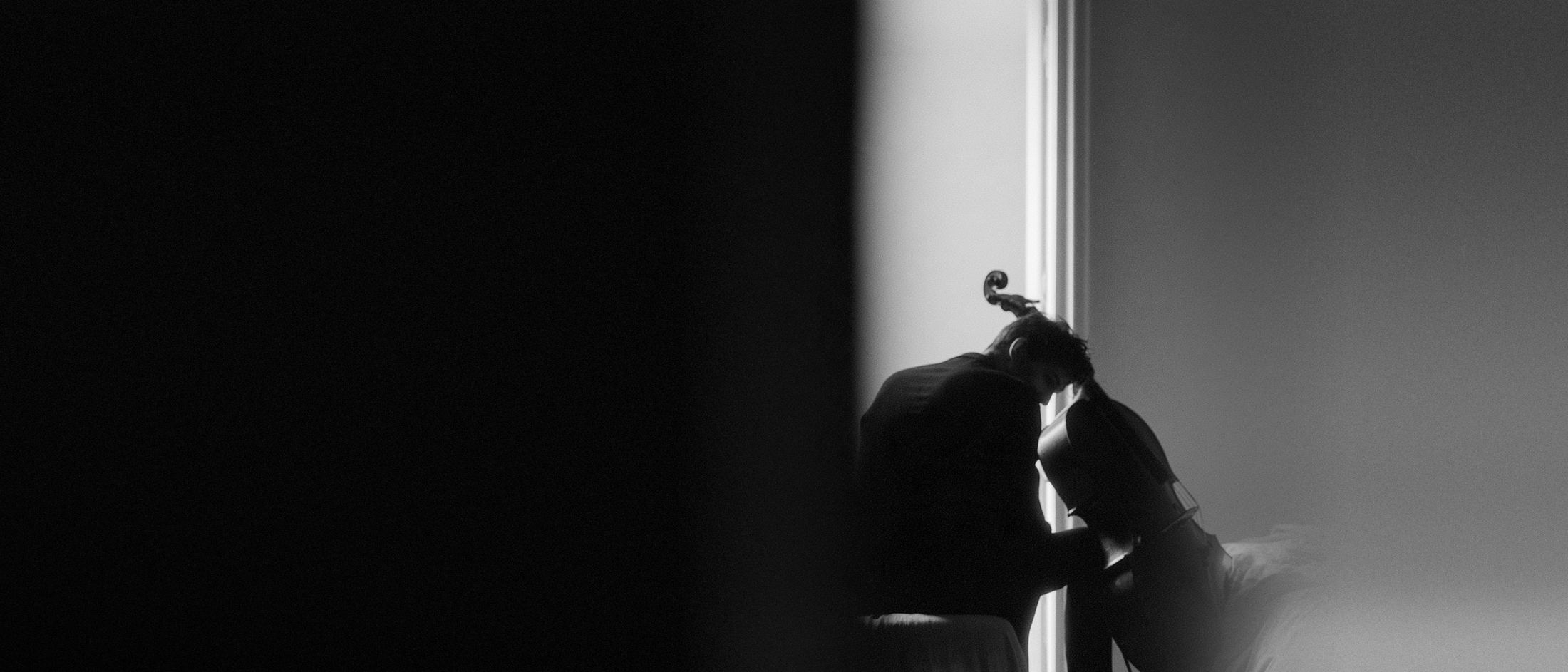 A cellist playing by a tall window, in black and white